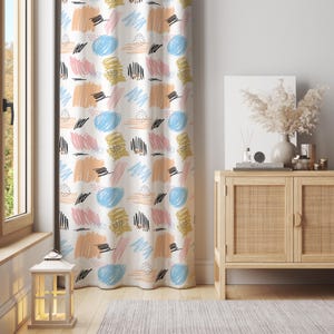 May include: White curtain with a colorful abstract pattern. The design features brushstrokes and shapes in shades of blue, pink, yellow, orange, and black. The curtain is hanging in front of a window, with a wooden cabinet and decor in the background.