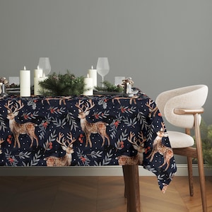 May include: A navy blue tablecloth with a repeating pattern of deer, leaves, and berries. The table is set with candles, glasses, and decorative greenery, creating a festive holiday atmosphere. A modern chair is positioned to the right.