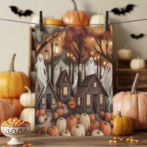 May include: A Halloween-themed print featuring a spooky forest scene with wooden houses, ghosts, and pumpkins. The artwork is held by a black clip on a string. The color palette includes orange, brown, and white, creating a festive autumn atmosphere.