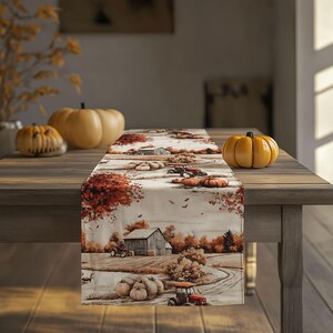 Peut inclure: Chemin de table rectangulaire avec une scène de récolte d'automne représentant une grange, des citrouilles et des tracteurs dans des tons orange, marron et beige. Le chemin de table est sur une table en bois avec des citrouilles.