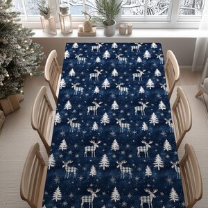May include: A navy blue tablecloth featuring a repeating pattern of white reindeer, Christmas trees, and snowflakes. The reindeer have a plaid design. The tablecloth is on a wooden table with six wooden chairs. A Christmas tree is visible.