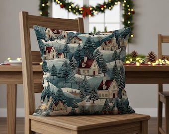 May include: A decorative throw pillow featuring a winter village scene. The pillow has a repeating pattern of houses with red roofs nestled among snow-covered hills and evergreen trees. The pillow is displayed on a wooden chair.