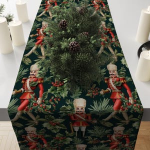 May include: A dark green table runner with a repeating pattern of red nutcracker soldiers and holly leaves. The runner features a central arrangement of greenery and pinecones, with white candles on either side. A festive holiday decoration.