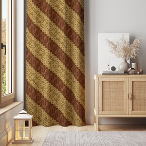 Könnte beinhalten: Ein brauner und goldfarbener Vorhang mit einem sich wiederholenden diagonalen Muster. Das Muster zeigt eine Reihe von ovalen Formen und geschwungenen Linien. Der Vorhang hängt vor einem Fenster, mit einem Holzschrank und dekorativen Gegenständen im Hintergrund.