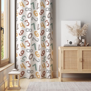 May include: A white curtain featuring a repeating pattern of colourful numbers in various sizes and fonts. The numbers are in shades of brown, yellow, green, and grey. The curtain hangs in front of a window and a wooden cabinet.