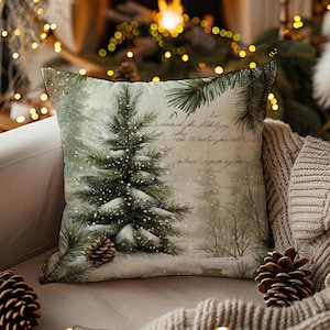 May include: Square decorative pillow with a winter forest scene. The pillow features a snow-covered evergreen tree, pine cones, and handwritten script. The color palette includes shades of green, white, and gray, evoking a cozy, seasonal feel. The pillow is likely used for home decor.