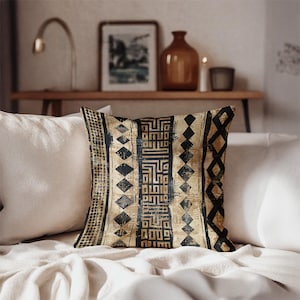 May include: Square throw pillow with a geometric pattern in black and tan. The design includes diamond shapes, vertical stripes, and a central block of stylized text. The pillow is placed on a white surface.