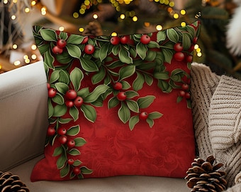 May include: A square decorative pillow with a festive Christmas design. The pillow features a red background with a pattern and a detailed illustration of green leaves and red berries. The pillow is placed on a light-colored sofa.