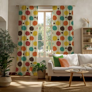 May include: A pair of beige curtains with a repeating pattern of large, colorful circles in shades of red, orange, yellow, teal, and brown. The curtains hang in front of a window, with a white sofa and wooden table in the foreground.