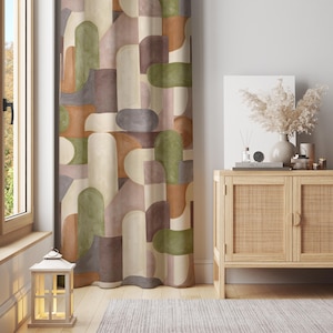 May include: A patterned curtain with a geometric design in shades of brown, green, and beige. The curtain hangs next to a window and a wooden cabinet with decorative items. A lit lantern sits on the floor.