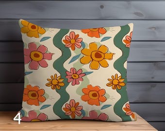 May include: Square decorative pillow with a floral pattern. The pillow features a cream background with orange, yellow, and pink flowers, green wavy lines, and blue leaves. The pillow is placed on a wooden surface.