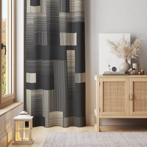 Puede incluir: Una cortina estampada con un diseño geométrico en tonos grises, negros y beige. La cortina cuelga frente a una ventana, con una linterna de madera en el suelo. A la derecha hay un mueble de madera con objetos decorativos.