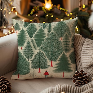 Pode incluir: Almofada decorativa com um padrão de floresta, apresentando árvores verdes e uma pessoa com um casaco vermelho. A almofada tem um fundo creme e está sobre um sofá neutro. Um item de decoração festivo.