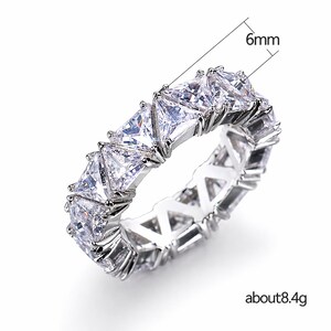Puede incluir: Un anillo plateado con una fila continua de piedras claras talladas en forma triangular. El anillo mide aproximadamente 6 mm de ancho y pesa unos 8,4 gramos. Las piedras est&aacute;n engastadas juntas, creando un dise&ntilde;o brillante.