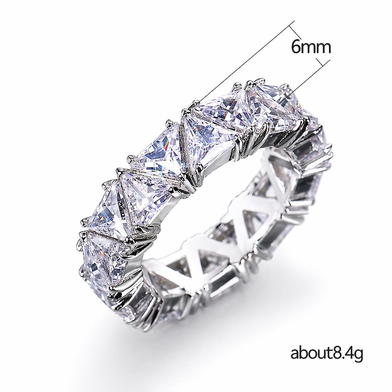 Puede incluir: Un anillo plateado con una fila continua de piedras claras talladas en forma triangular. El anillo mide aproximadamente 6 mm de ancho y pesa unos 8,4 gramos. Las piedras est&aacute;n engastadas juntas, creando un dise&ntilde;o brillante.