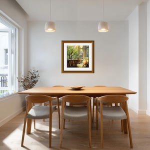 May include: A framed artwork depicting a cozy reading nook with a window view of a lush green tree. The artwork is displayed above a wooden dining table with six chairs. The room has white walls and pendant lights.
