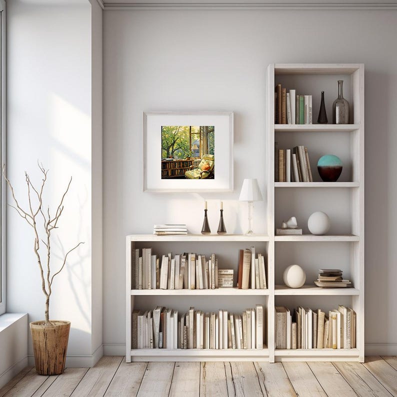 May include: A bright, airy room with white bookshelves filled with books. A framed picture hangs on the wall, depicting a cozy reading nook. A decorative tree in a wooden pot stands near a large window, and a small lamp sits on a shelf.