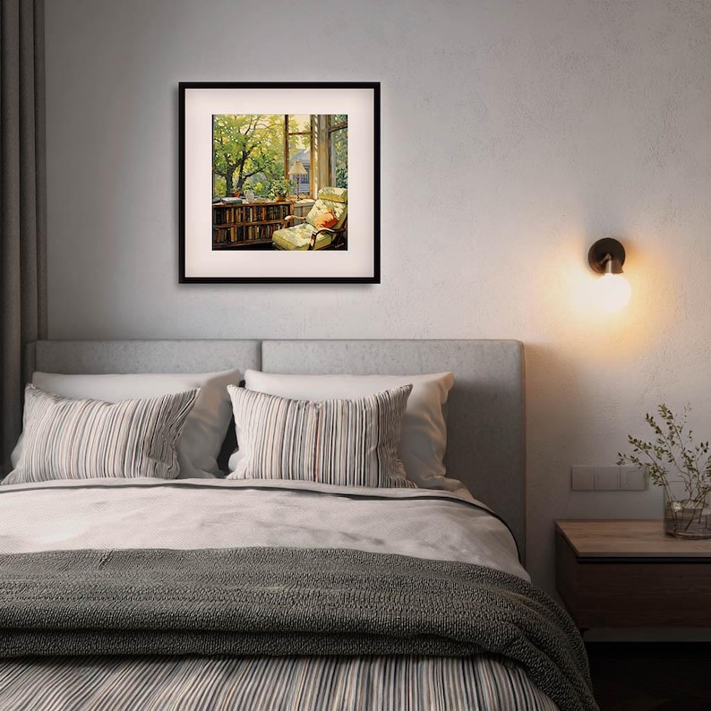 May include: A framed print of a cozy reading nook with a window view. The artwork depicts a room with a bookshelf, armchair, and a window overlooking a lush green tree. The frame is black, and the scene is illuminated by natural light.