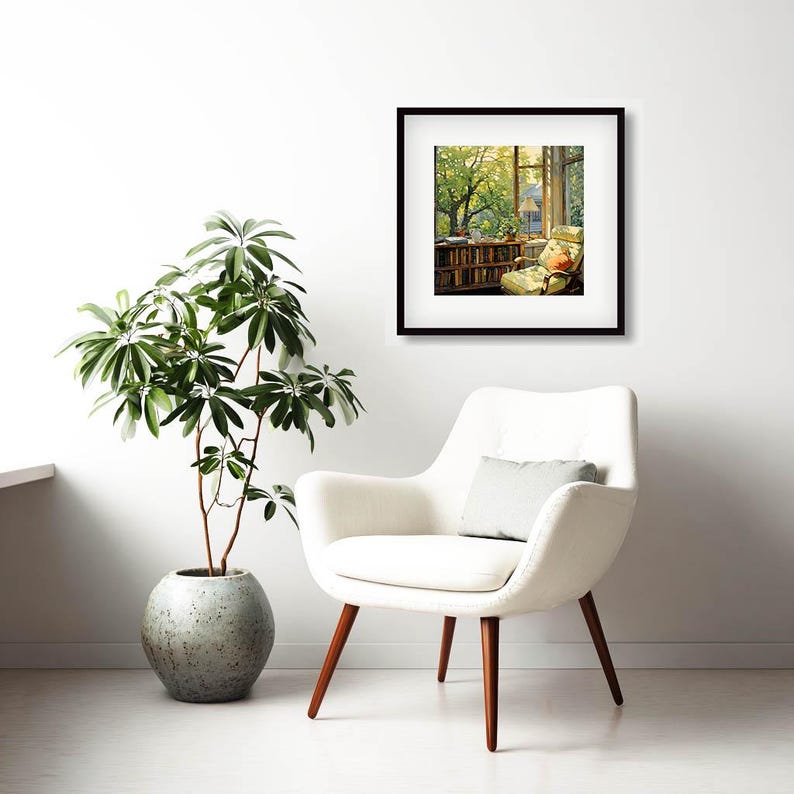 May include: A framed artwork depicting a cozy reading nook with a window view of a lush green tree. A white armchair with wooden legs and a gray pillow sits in front of the artwork. A potted plant with large green leaves is to the left.