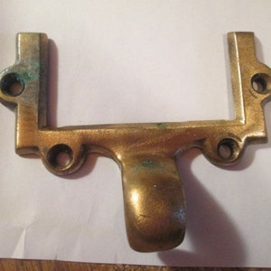 May include: A gold-toned metal door handle with a rectangular frame and a curved bottom. The handle has a worn, aged look.