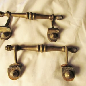 May include: Two antique brass drawer pulls. Each pull has a cylindrical handle with ribbed ends and a curved bracket. The pulls are a warm, aged brass color, showing signs of wear.