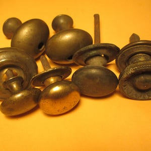 May include: A collection of antique brass door knobs and hardware, in various shapes and sizes. The knobs have a tarnished, aged appearance, with visible wear and patina. Some knobs have a round, oval, or mushroom shape.