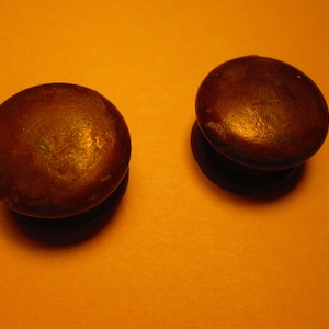 May include: Two round, dark brown wooden cabinet knobs with a slightly glossy finish. The knobs are set against an orange background, and each has a short, cylindrical base. The knobs are likely for furniture.