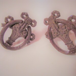 May include: Two ornate metal drawer pulls with a ring handle and a floral design. The pulls are a dark brown color.