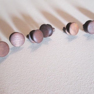 May include: A collection of 10 brown wooden knobs with a metal screw on the back. The knobs are arranged in a row on a white surface.