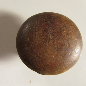 May include: A round, wooden knob with a dark brown finish. The knob has a smooth, rounded top and a slightly textured surface. The wood grain is visible, adding to its rustic appearance. The knob is likely for a cabinet or drawer.