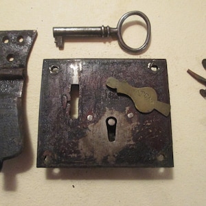 May include: A dark metal rim lock with a keyhole and a brass cover plate marked PATENT, accompanied by a matching iron key, a vertical hinge strap with three screw holes, and a collection of small iron nails scattered to the right side.
