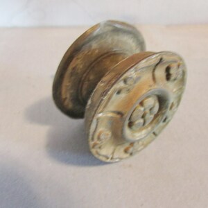 May include: Antique brass-toned cabinet knob with a decorative floral design. The knob features a rounded shape with a detailed face and a cylindrical base. The aged finish gives it a vintage look, suitable for furniture restoration.