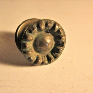 May include: Antique brass door knob with a circular design. The knob features a central rounded area surrounded by a decorative, textured border. The brass has a slightly aged, tarnished appearance, adding to its vintage charm.