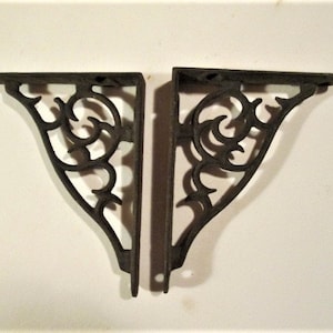 May include: Two black metal shelf brackets with a decorative scroll design. The brackets are made of cast iron and have a rustic finish.