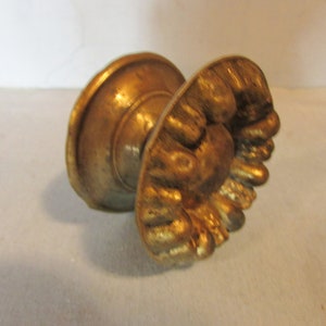 May include: A gold-colored, antique-style door knob. The knob has a round base and a decorative, ornate handle with a textured, floral design. The hardware is likely made of brass or a similar metal.