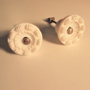 May include: Two white ceramic drawer knobs with a decorative floral design and a brass screw.
