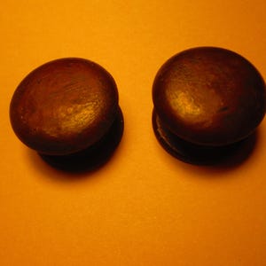 May include: Two dark brown, round wooden cabinet knobs with a slightly domed top and a flat base. The knobs are set against an orange background, creating a warm, inviting aesthetic. These knobs are ideal for furniture restoration or new builds.