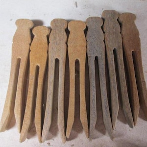 May include: A collection of eight vintage wooden clothespins. Each pin is a light brown color, with a rounded top and a split design for gripping clothes. The pins vary slightly in color, showing signs of age and use.