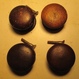 May include: Four antique wooden caster wheels with screws. Two are a dark brown with a mottled appearance, and two are a lighter brown with visible wood grain. The screws are metal and have a rusty appearance.