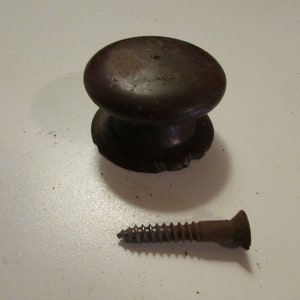May include: A dark brown wooden cabinet knob with a rounded top and a decorative base, accompanied by a rusty brown screw. The knob is likely for furniture or a drawer.