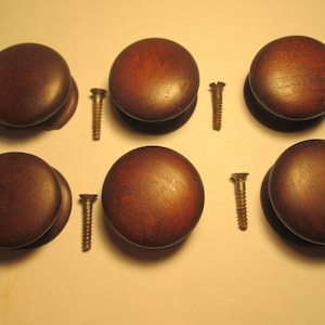 May include: A set of six round, dark brown wooden cabinet knobs with a smooth, polished finish. Each knob is accompanied by a matching metal mounting screw, arranged in two rows of three to display the hardware components clearly.