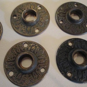 May include: A collection of antique bronze-toned metal hardware pieces. Each piece features a circular design with an embossed floral pattern and a central hole, along with smaller holes around the perimeter. The hardware has a vintage aesthetic.