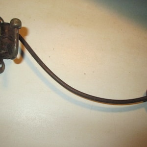 May include: An antique, dark brown metal coat hook. The hook has a decorative bracket with two screw holes, a curved arm, and a round knob at the end. The metal has a slightly aged appearance.