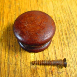 May include: A round, dark brown wooden cabinet knob with a matching base and a rusty screw. The knob is a classic design, likely for a drawer or cabinet door. The screw is a standard size for attaching the knob.