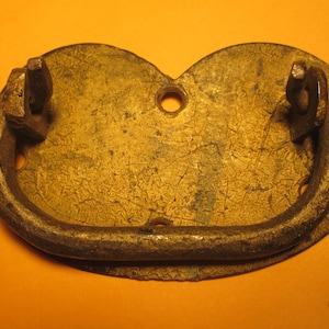 May include: A weathered brass-toned metal drawer pull featuring a heart-shaped backplate with a textured, distressed surface. The hardware includes a hinged, semi-circular drop handle attached to two mounting points and two circular screw holes.