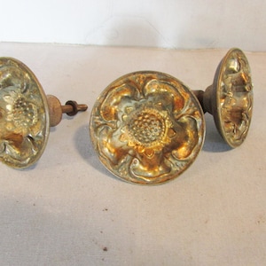 May include: Three antique brass door knobs with a floral design. The knobs have a tarnished gold finish and are oval and round in shape. The hardware is likely vintage and adds a classic touch to any door.