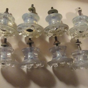 May include: Set of eight clear glass cabinet knobs with a frosted finish and a decorative, scalloped edge. Each knob has a metal post for attaching to a cabinet door.