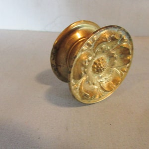 May include: A vintage brass door knob with an ornate floral design. The knob has a rounded shape with a detailed flower and leaf pattern on the front. The brass has a warm, aged patina.
