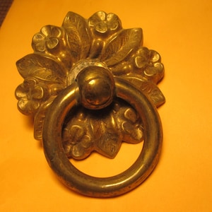 May include: Ornate brass door knocker with a floral design. The knocker features a large ring handle and is mounted on a decorative floral base. The brass has a warm, aged patina.