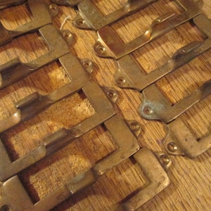 May include: A set of 10 antique brass drawer pulls with a rectangular shape and a simple design. The pulls have a slightly aged finish and are perfect for adding a vintage touch to any furniture.